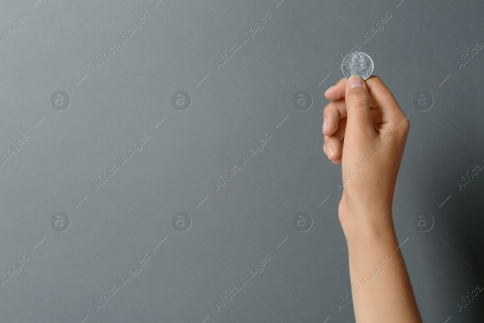 Photo of Young woman holding coin on grey background, closeup. Space for text