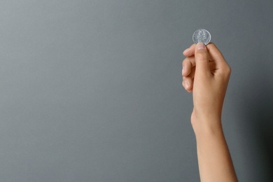 Young woman holding coin on grey background, closeup. Space for text