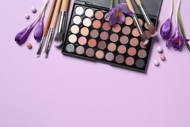 Photo of Flat lay composition with eyeshadow palette and beautiful crocuses on lilac background, space for text