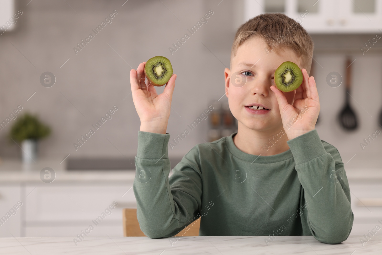 Photo of Cute boy with fresh kiwi at table in kitchen