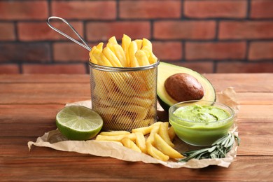 Parchment with french fries, guacamole dip, lime and avocado served on wooden table