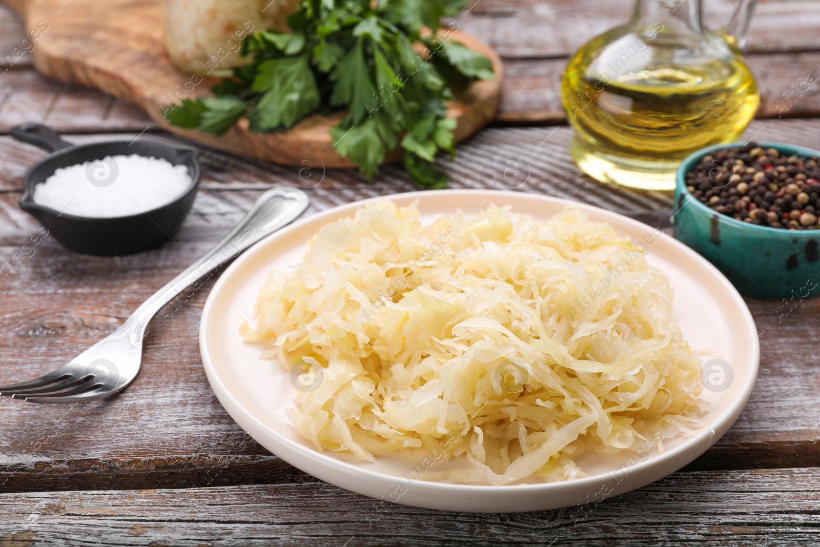 Photo of Plate of tasty sauerkraut and ingredients on wooden table