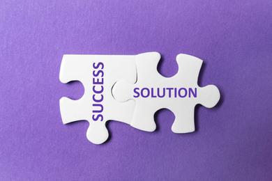 Image of Unfitting white puzzle pieces with words SUCCESS and SOLUTION on purple background, top view