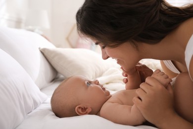 Happy young mother with her cute baby on bed indoors