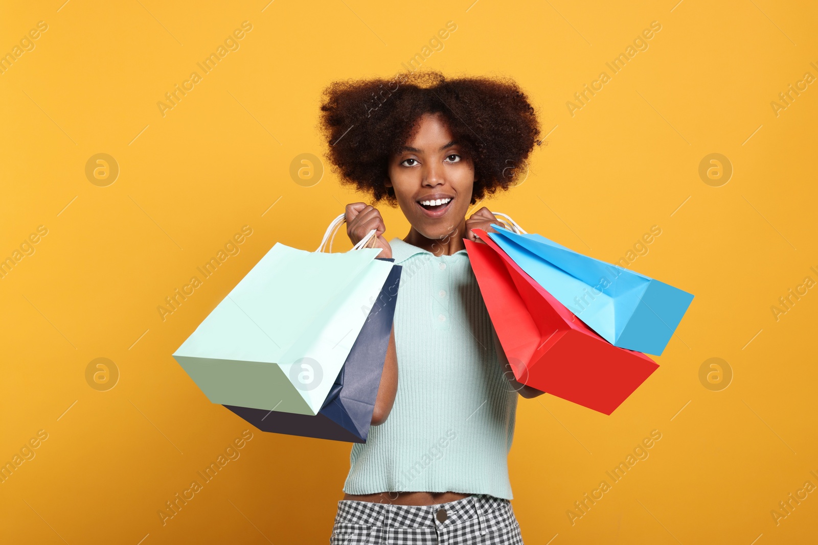 Photo of Happy African American woman with shopping bags on orange background