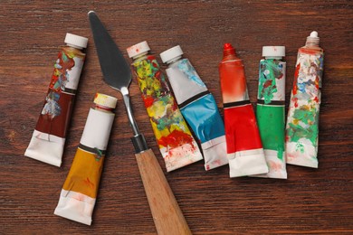 Tubes with oil paints and spatula on wooden table, flat lay