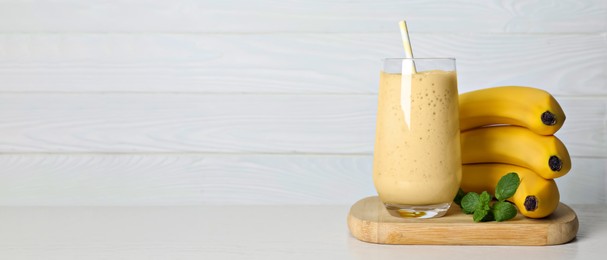 Image of Glass of tasty smoothie, mint and fresh bananas on white wooden table, space for text. Banner design
