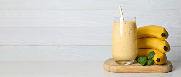 Glass of tasty smoothie, mint and fresh bananas on white wooden table, space for text. Banner design