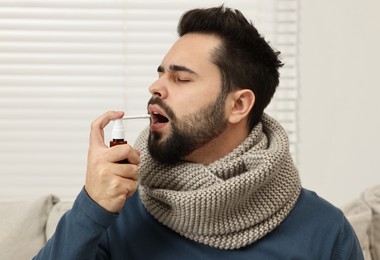 Young man with scarf using throat spray indoors