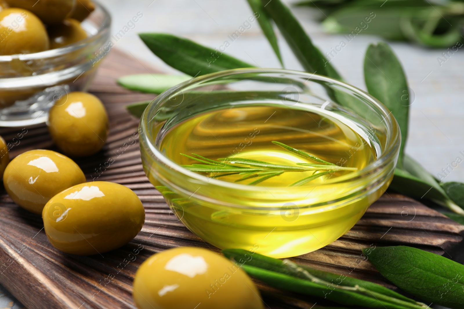 Photo of Bowl of cooking oil, olives and green leaves on wooden table, closeup