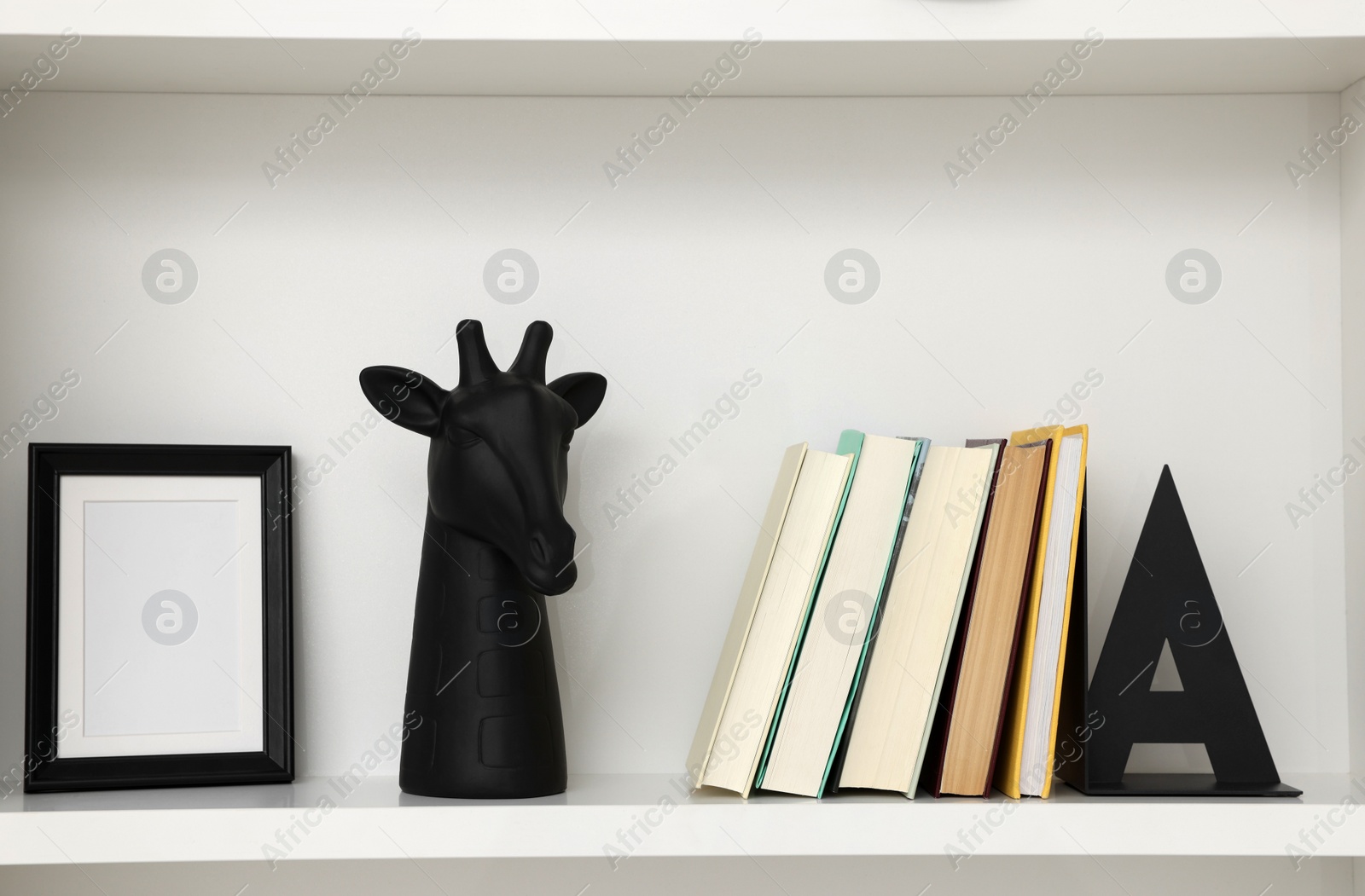 Photo of Books, decorative giraffe and frame on shelving unit