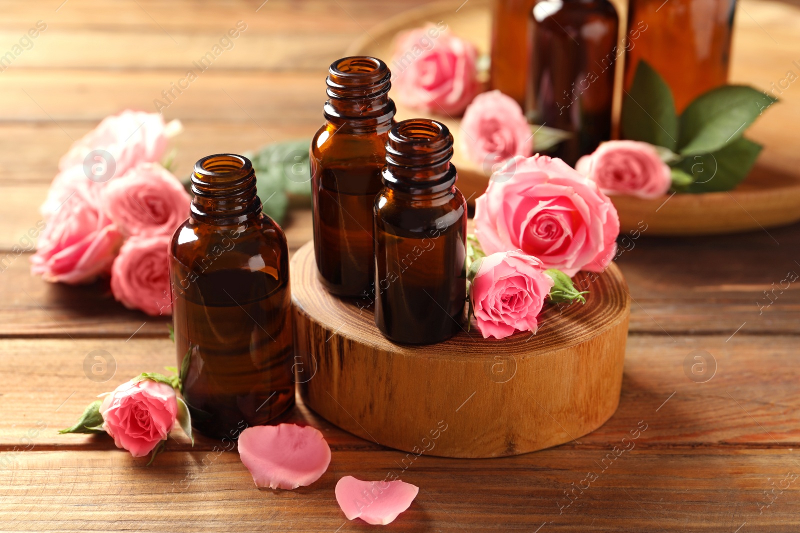 Photo of Bottles of rose essential oil and fresh flowers on wooden table