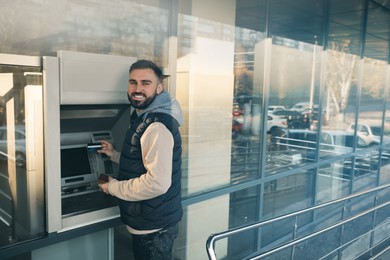Young man using cash machine for money withdrawal outdoors