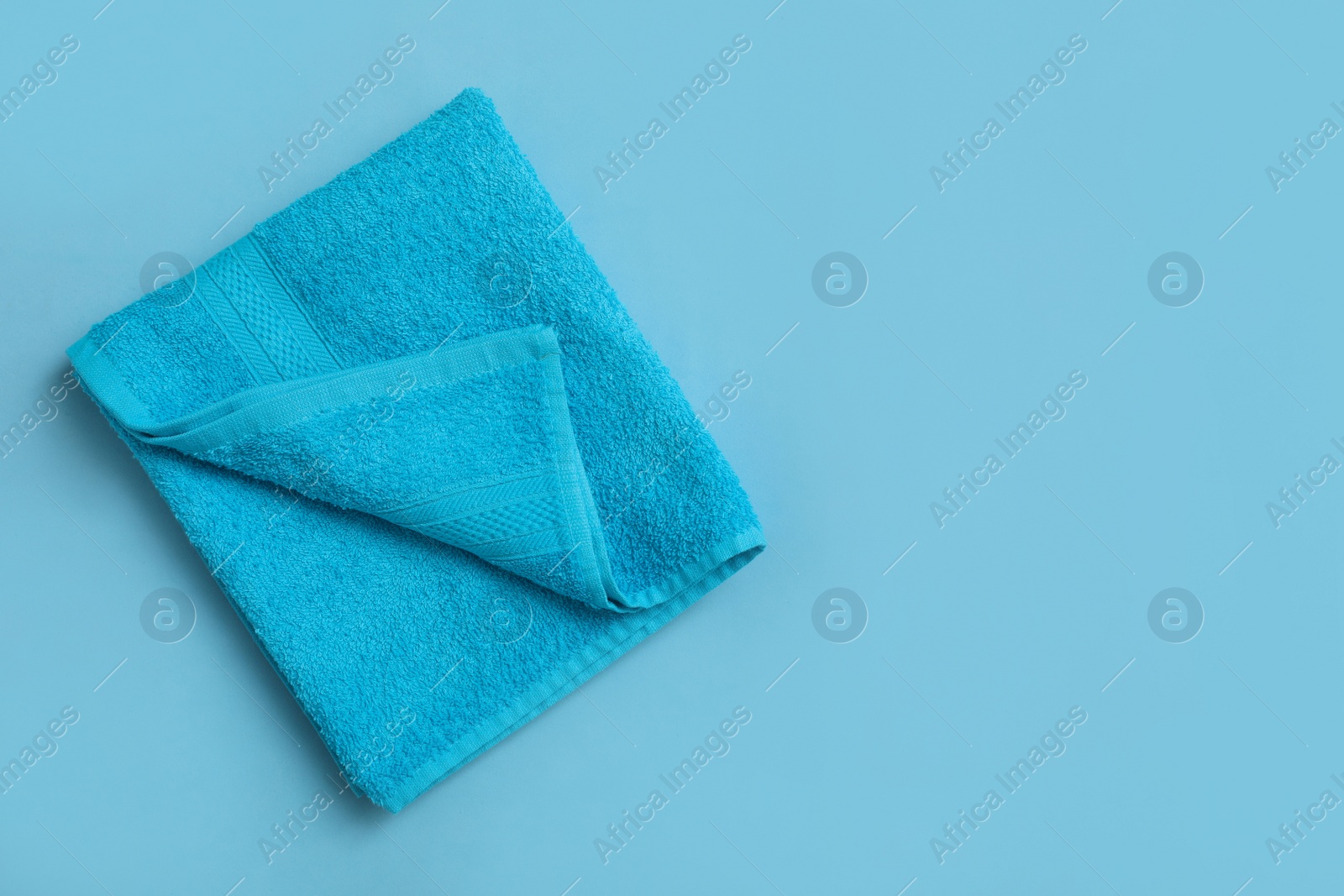 Photo of Folded soft beach towel on light blue background, top view. Space for text