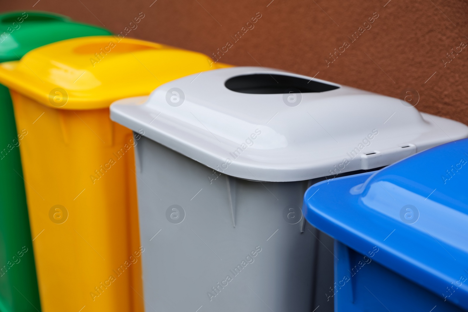 Photo of Many color recycling bins near brown wall, closeup