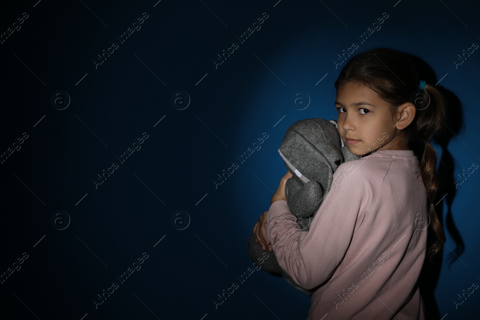 Photo of Sad little girl with toy near blue wall, space for text. Domestic violence concept