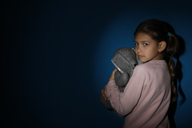 Photo of Sad little girl with toy near blue wall, space for text. Domestic violence concept