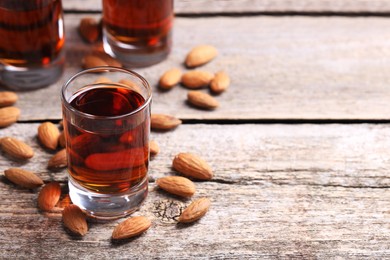 Shot glasses with tasty amaretto liqueur and almonds on wooden table, closeup. Space for text