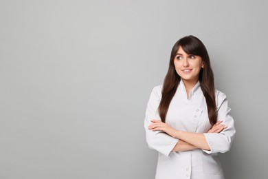 Cosmetologist in medical uniform on grey background, space for text