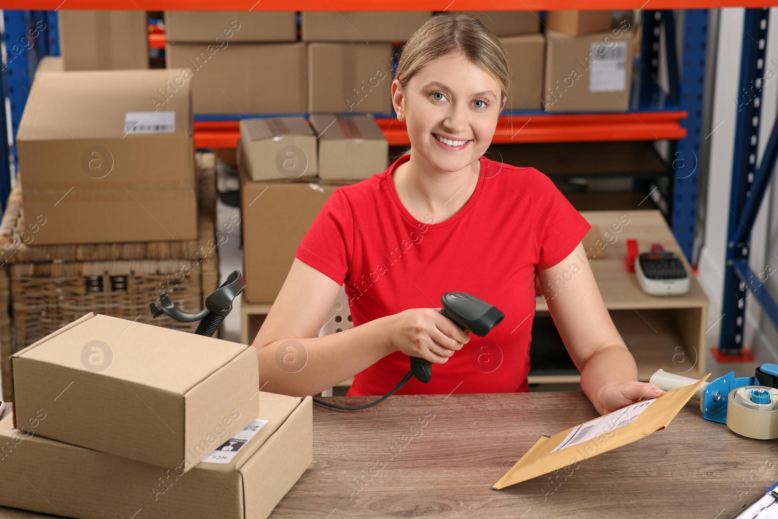 Photo of Post office worker with scanner reading parcel barcode at counter indoors