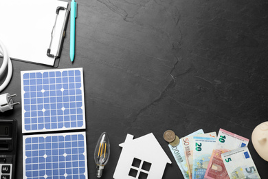 Photo of Flat lay composition with solar panels and money on black table. Space for text