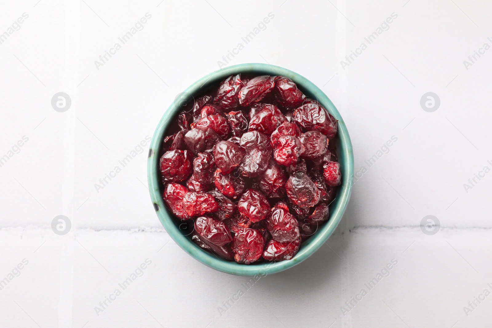 Photo of Tasty dried cranberries in bowl on white tiled table, top view