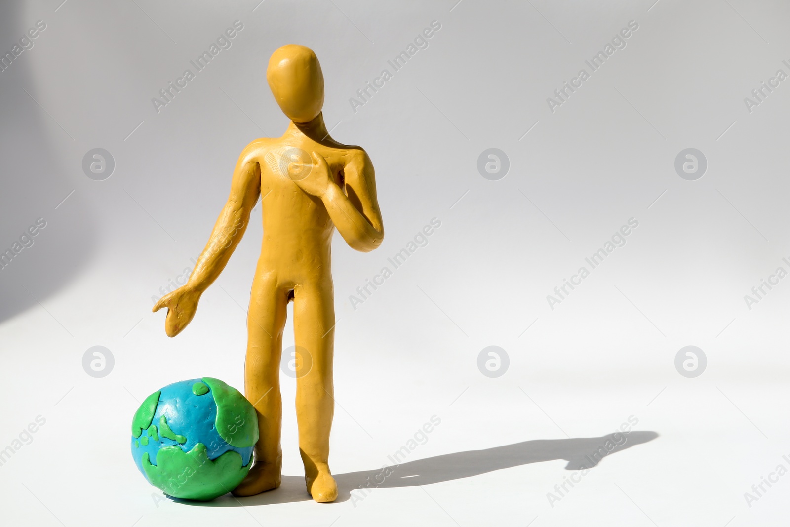 Photo of Yellow plasticine human figure with planet on white background, space for text