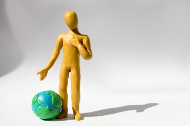 Photo of Yellow plasticine human figure with planet on white background, space for text