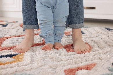 Photo of Mother supporting her baby son while he learning to walk on carpet indoors, closeup