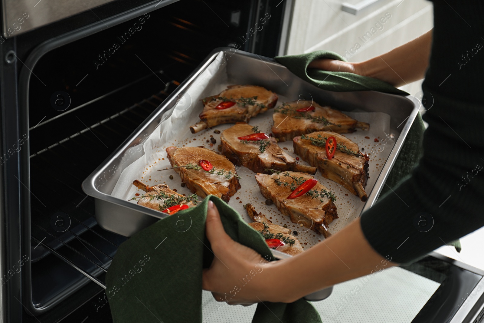 Photo of Woman taking delicious ribs out of oven, closeup