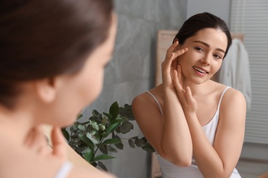 Photo of Young woman massaging her face near mirror in bathroom