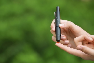 Photo of Woman using lancet pen on blurred background. Diabetes control