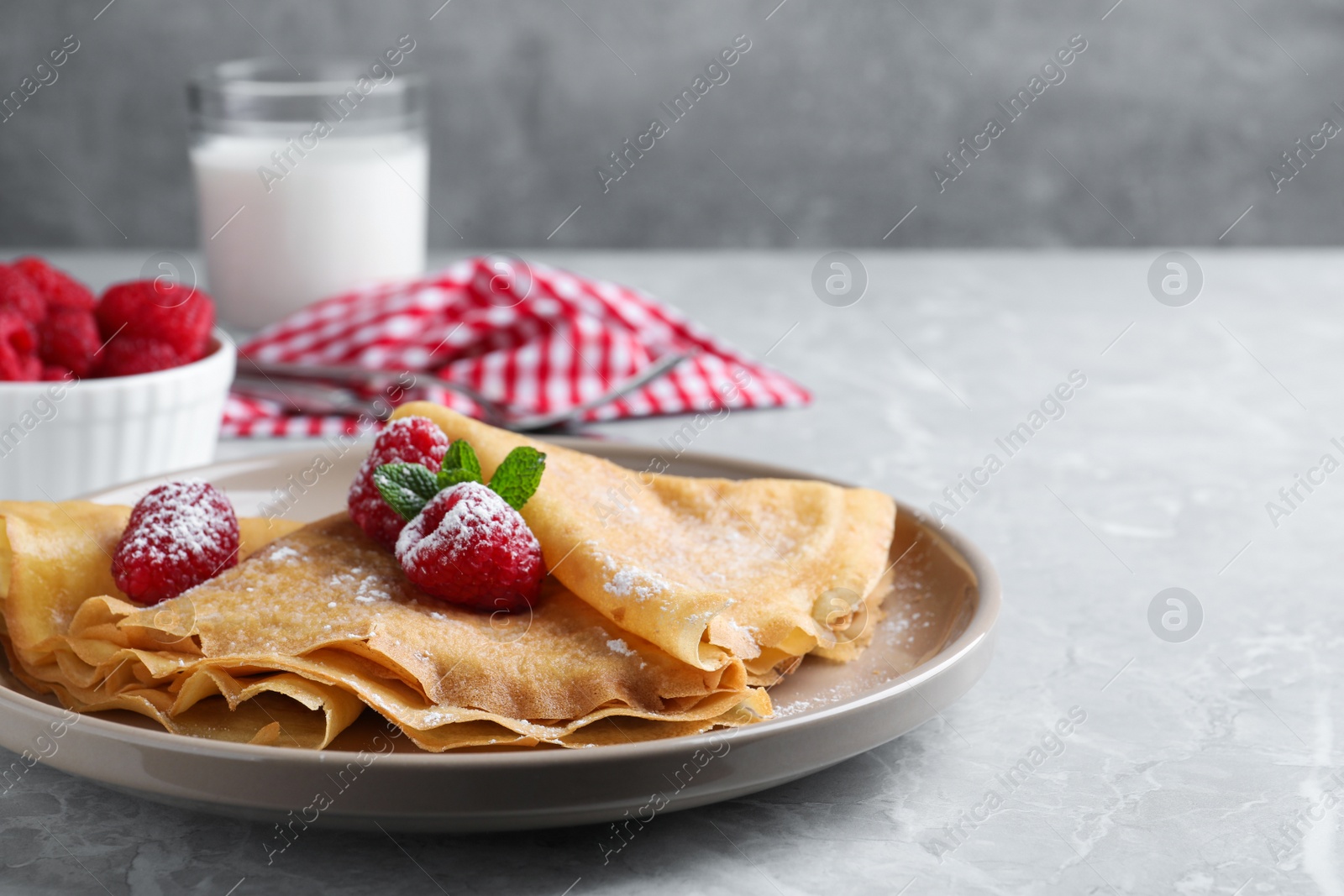 Photo of Delicious crepes served with mint, raspberries and powdered sugar on grey table. Space for text