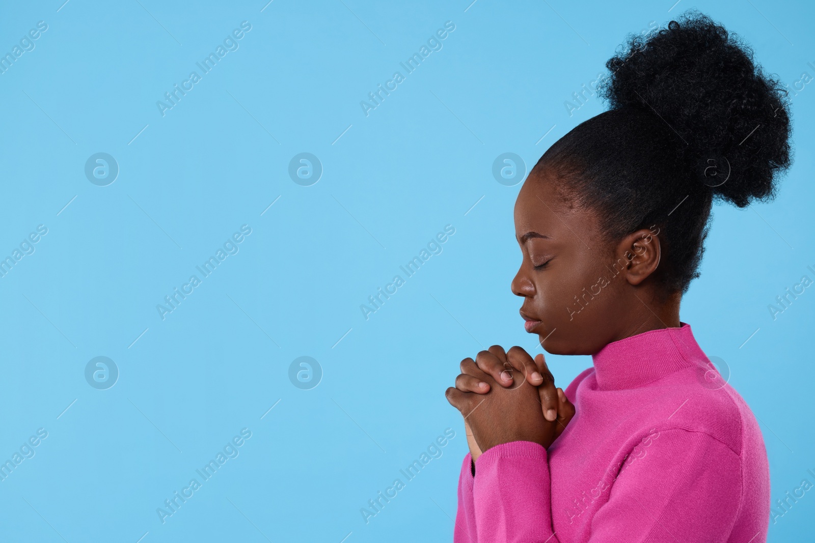 Photo of Woman with clasped hands praying to God on light blue background. Space for text