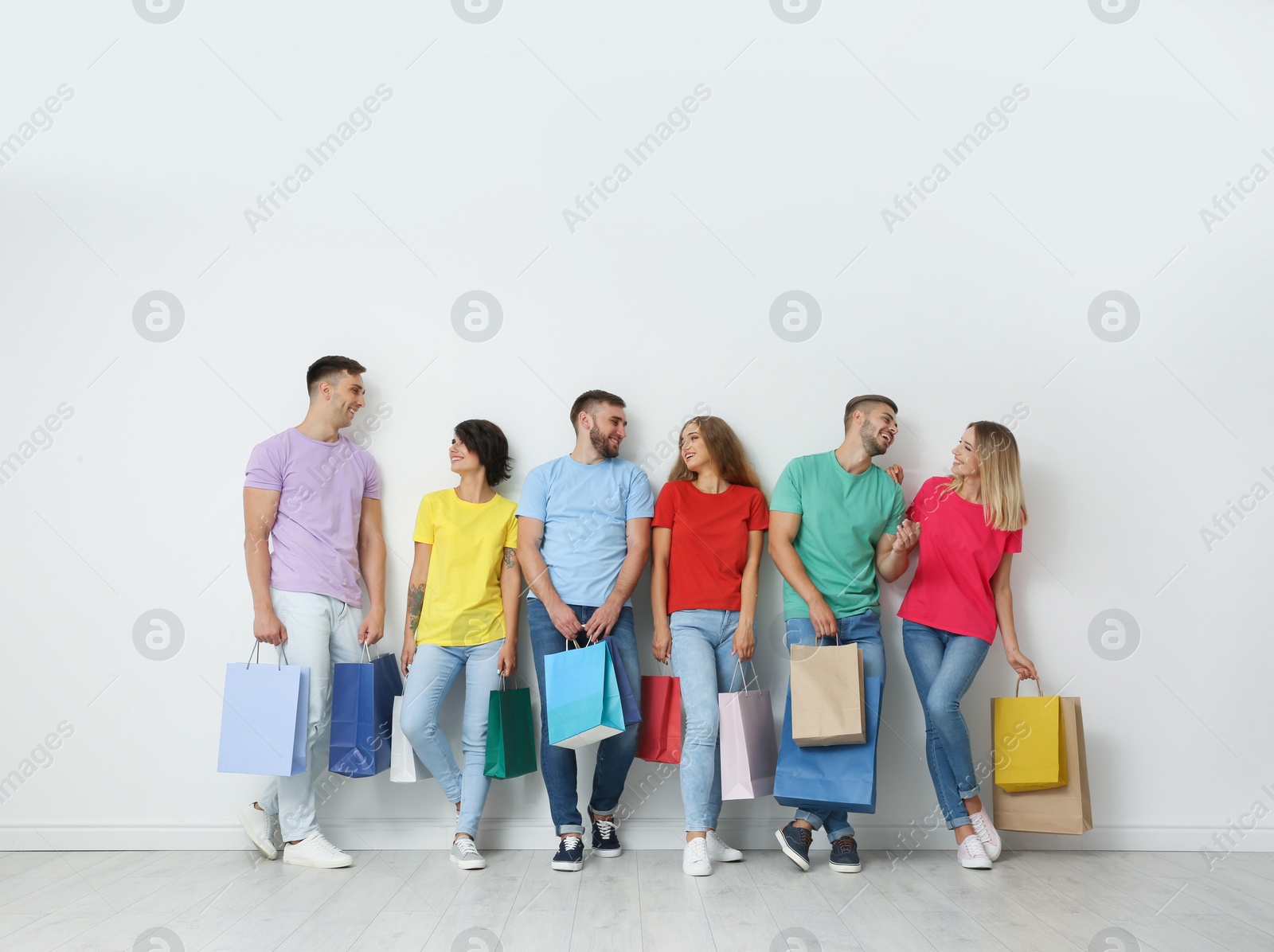 Photo of Group of young people with shopping bags near light wall