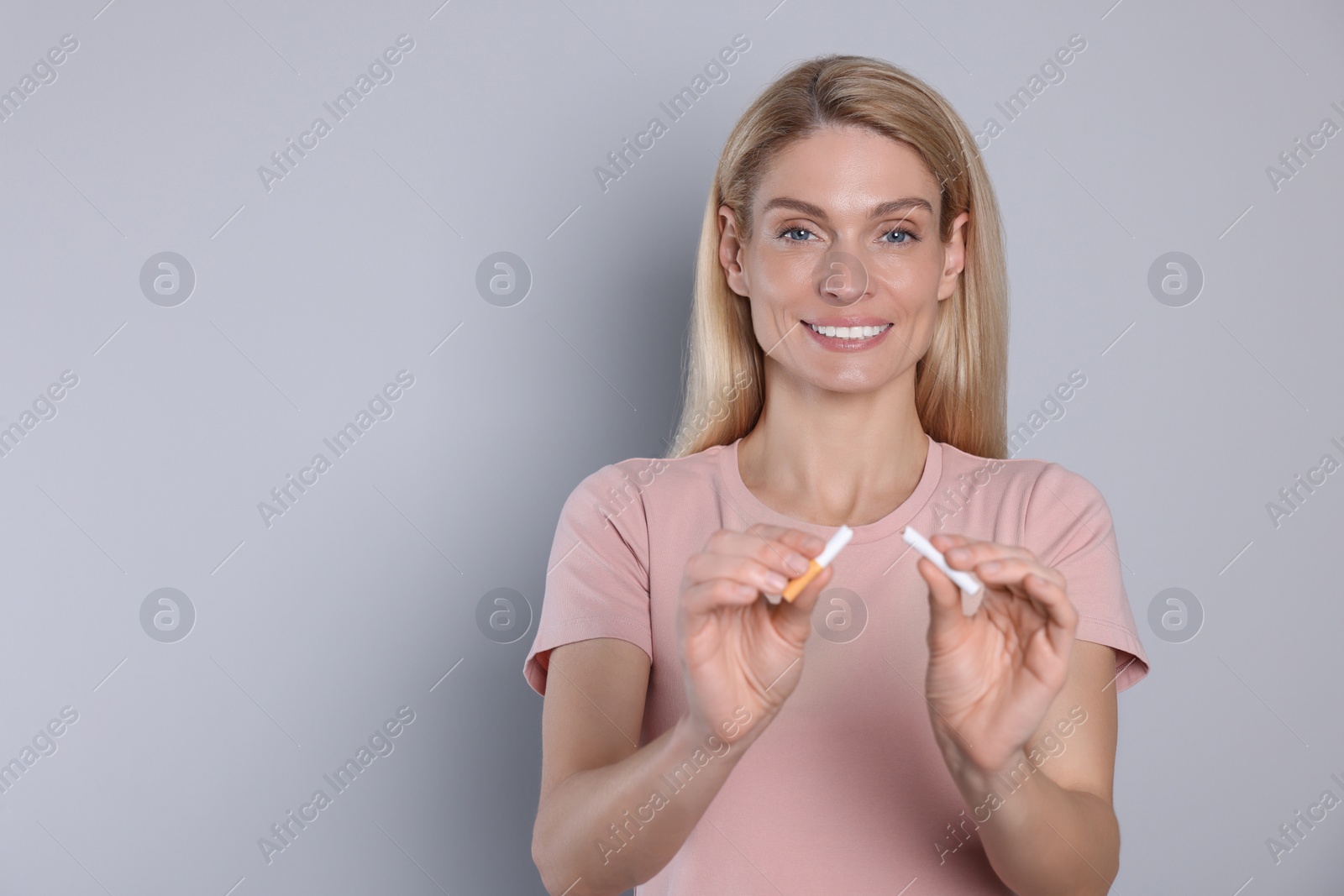 Photo of Stop smoking concept. Happy woman with broken cigarette on light grey background. Space for text