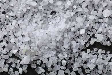 Scattered white natural salt on black table, top view