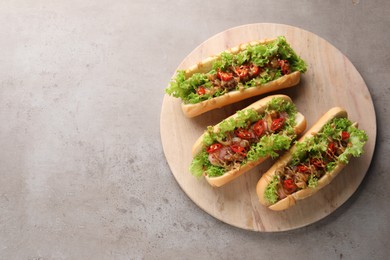 Tasty hot dogs with chili, lettuce and sauce on grey textured table, top view. Space for text