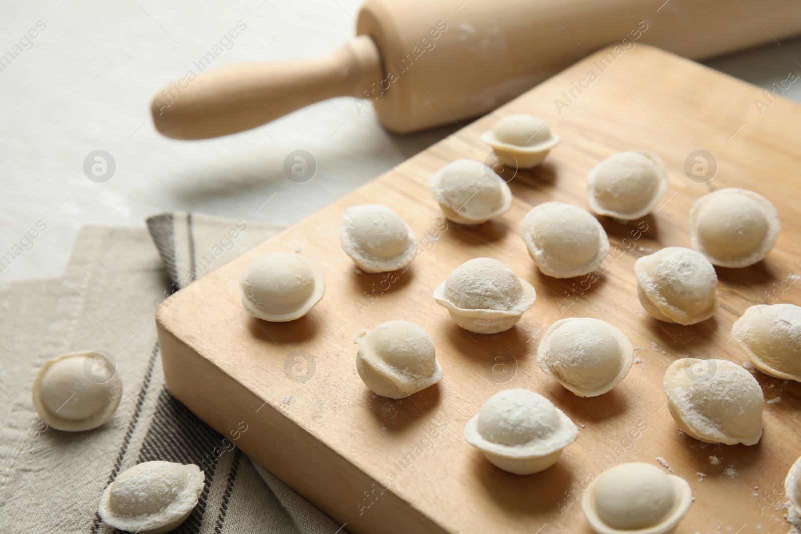 Photo of Board with raw dumplings and rolling pin on table, closeup