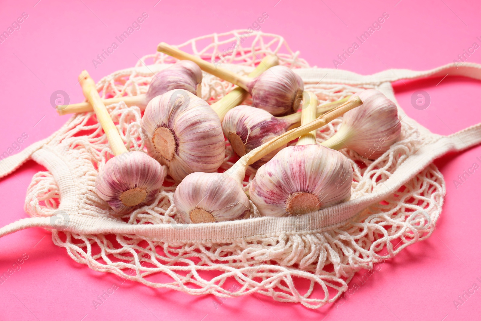 Photo of String bag with garlic heads on bright pink background, closeup