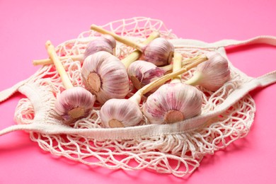 String bag with garlic heads on bright pink background, closeup