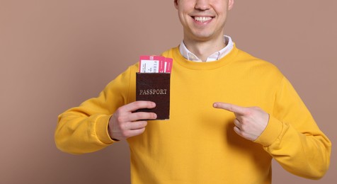 Smiling man pointing at passport and tickets on beige background, closeup