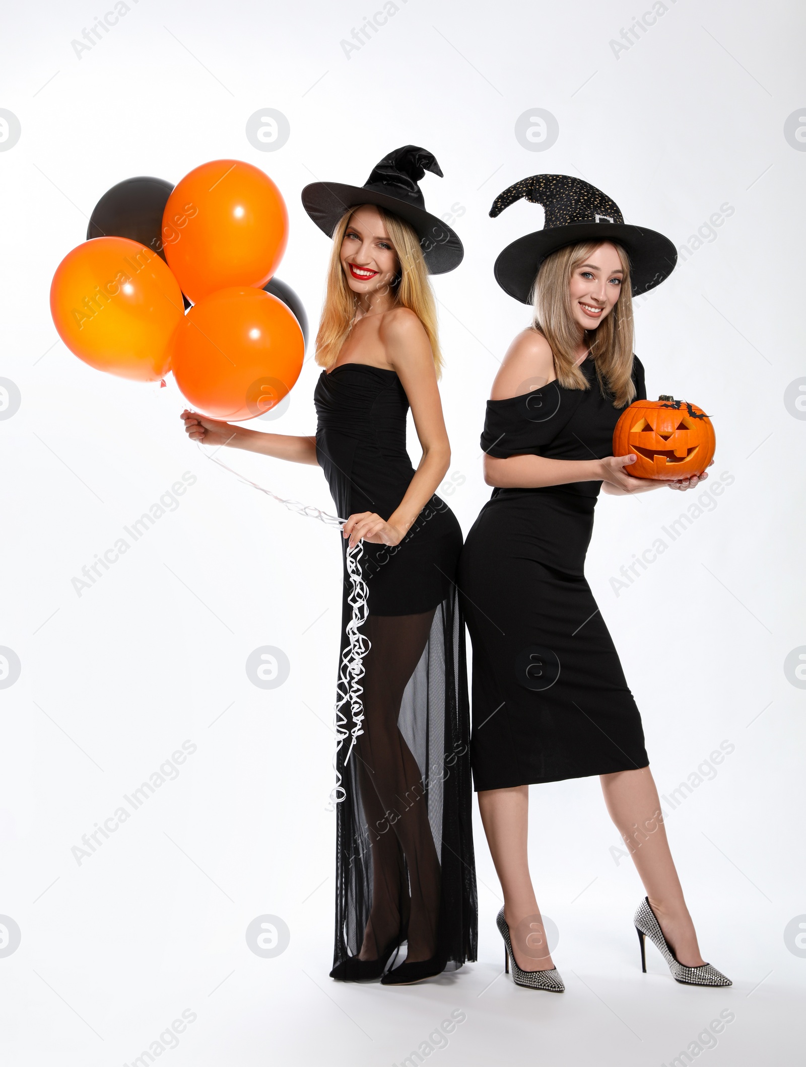 Photo of Beautiful women in witch costumes with balloons and jack o'lantern on white background. Halloween party