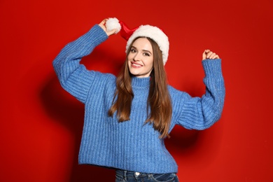 Photo of Young woman in Christmas sweater and Santa hat on red background