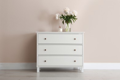 Photo of White chest of drawers with bouquet and candle near beige wall