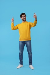 Photo of Smiling man taking selfie with smartphone on light blue background