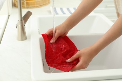 Photo of Woman washing beeswax food wrap under tap water in kitchen sink, closeup