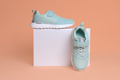 Pair of comfortable sports shoes and box on pale coral background