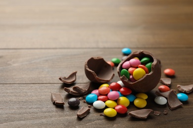 Photo of Broken chocolate egg and colorful candies on wooden table. Space for text