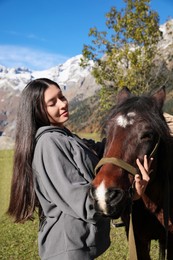 Photo of Young woman hugging horse in mountains on sunny day. Beautiful pet